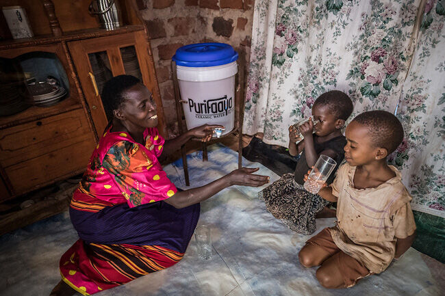 Mum with two children drinking clean water next to their ceramic water filter from Spouts.