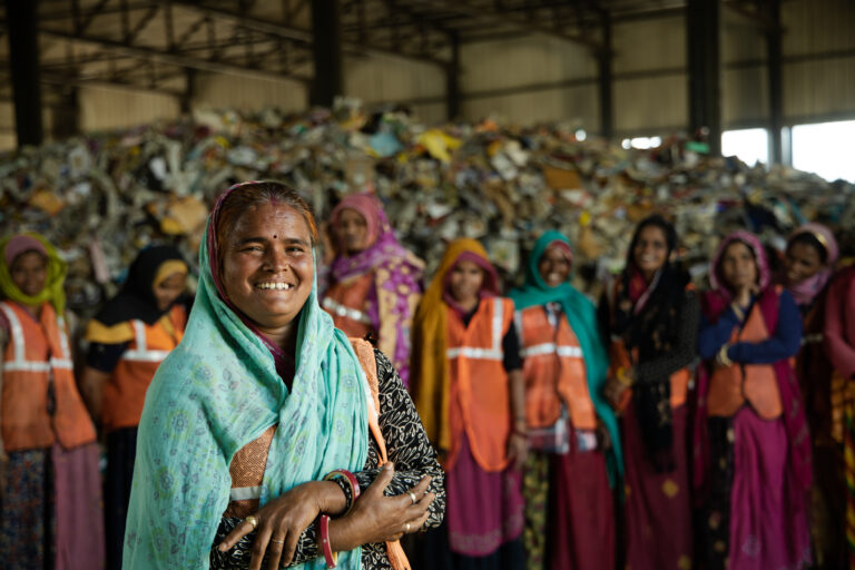 A line up of women waste workers smiling in front of a pile of waste they are sorting.