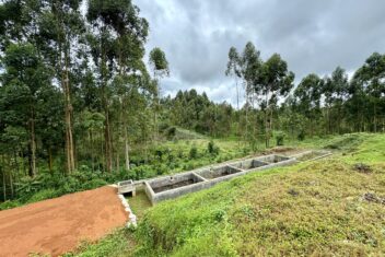 Green forested area in front a grass bank and faecal sludge treatment plant