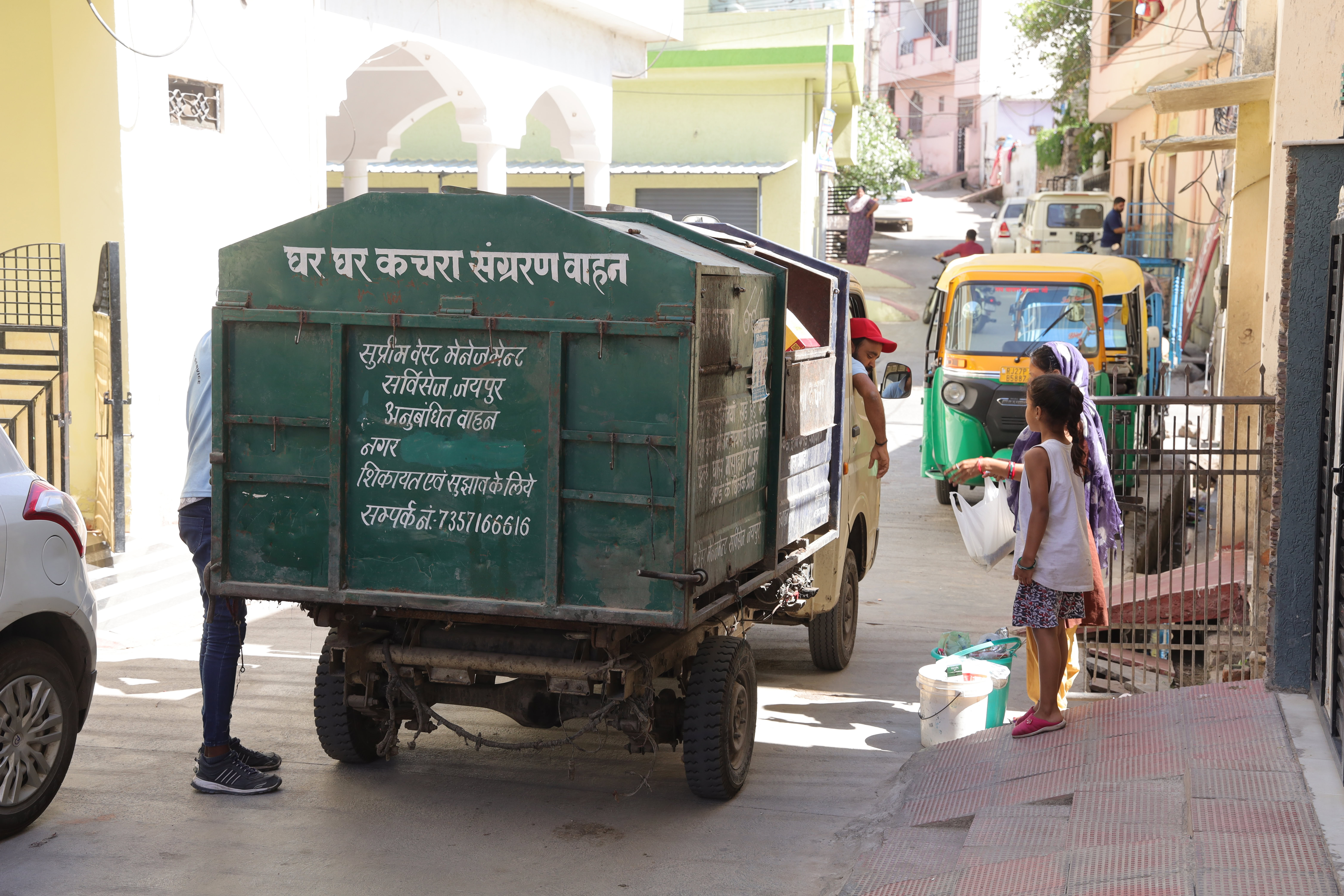 Green waste collection truck stopping at household and collecting waste from woman and child