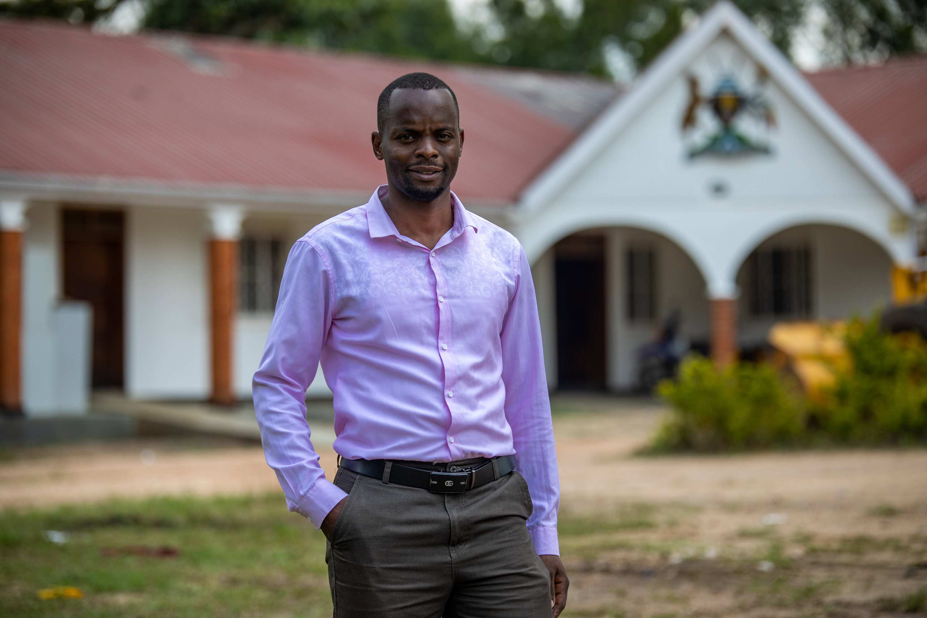 Agape in a pink shirt standing up in front of a red and white building 