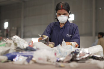 Woman sorting waste on conveyor belt with facemask