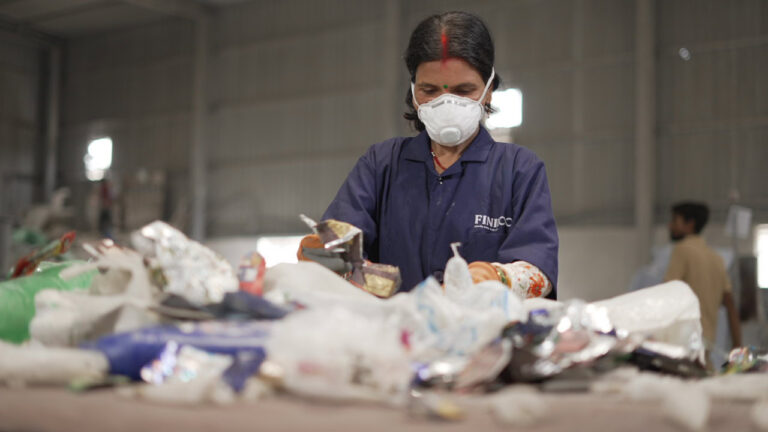 Woman sorting waste on conveyor belt with facemask